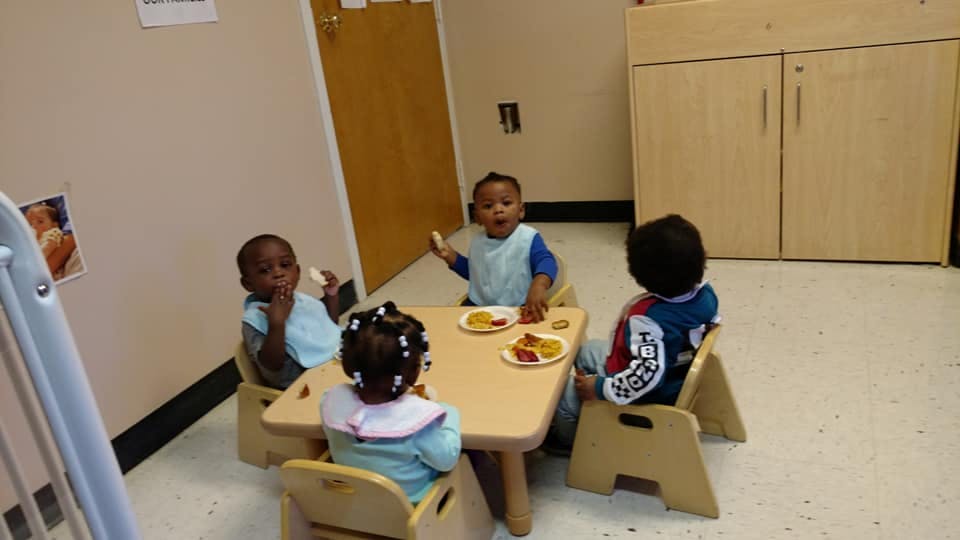 Four children eating at a small table in a classroom