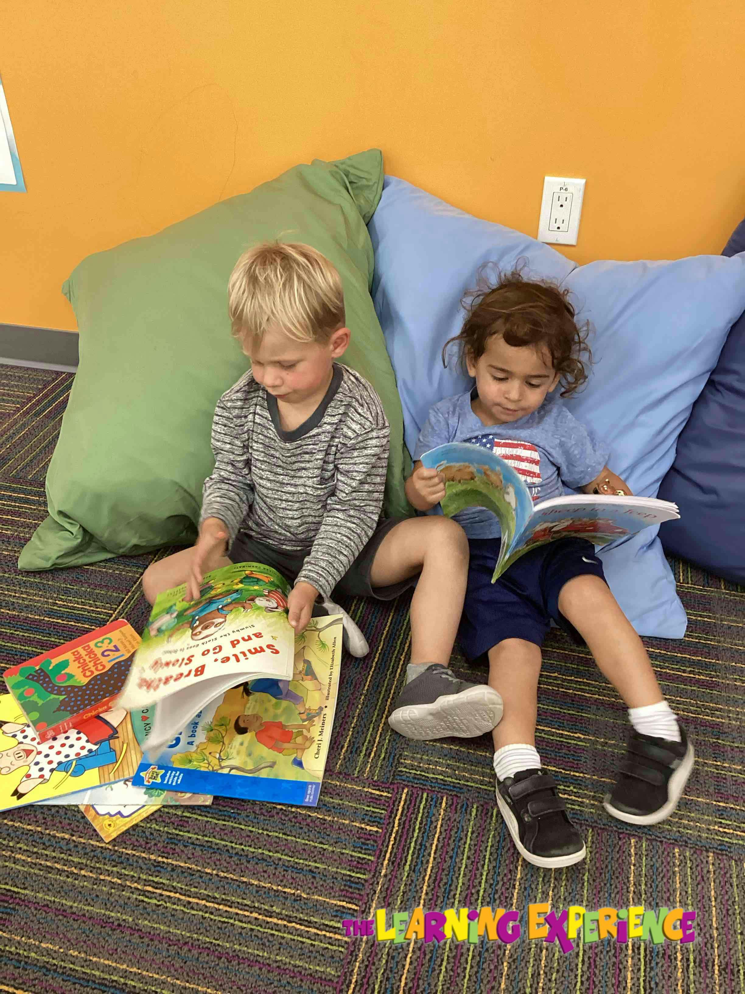 Two children sitting on the floor with pillows, reading books