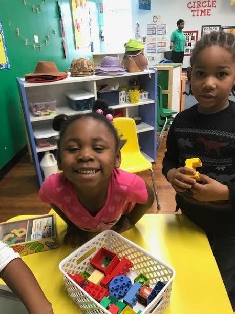 Two children at a table with a basket of building blocks