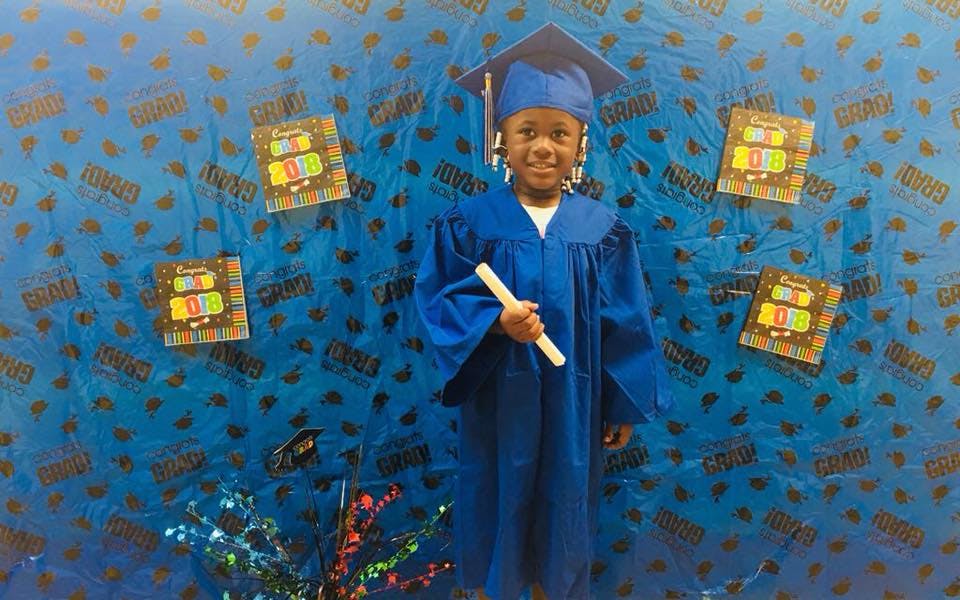 Child in blue graduation cap and gown holding a diploma