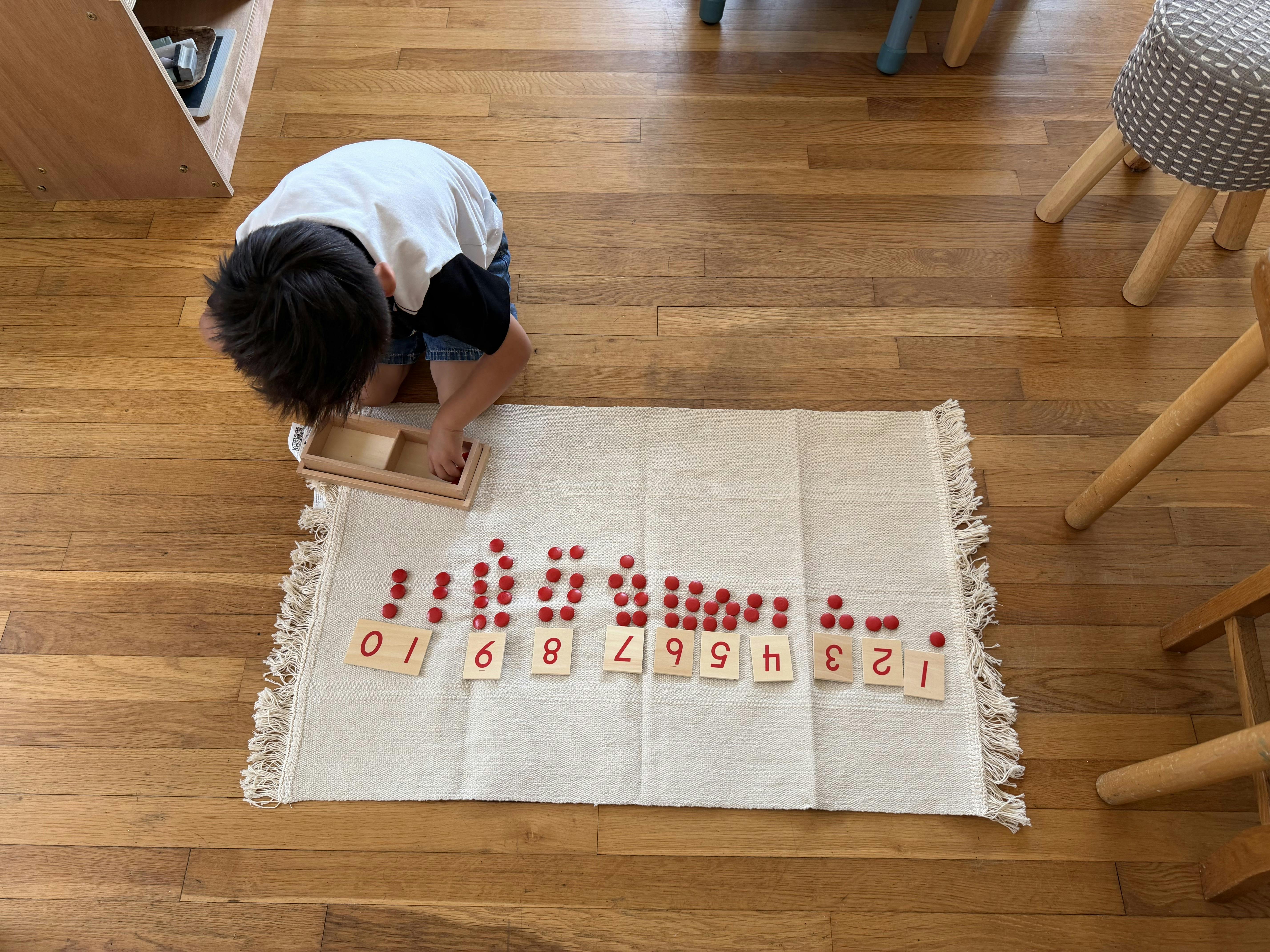 Child on knees sorting red math counters onto numbered wooden tiles