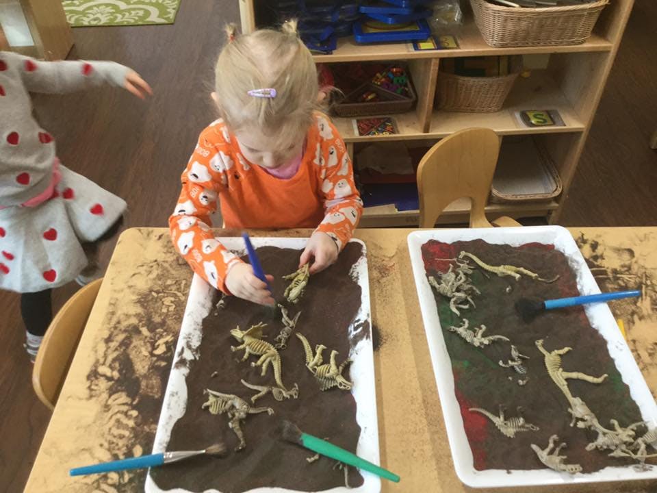 Child playing with dinosaur toys in a tray of sand