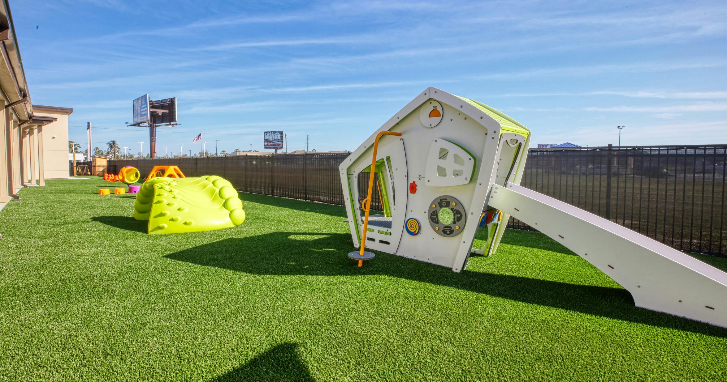 Playground with green turf, modern playhouse with slide, and soft play climbing structures