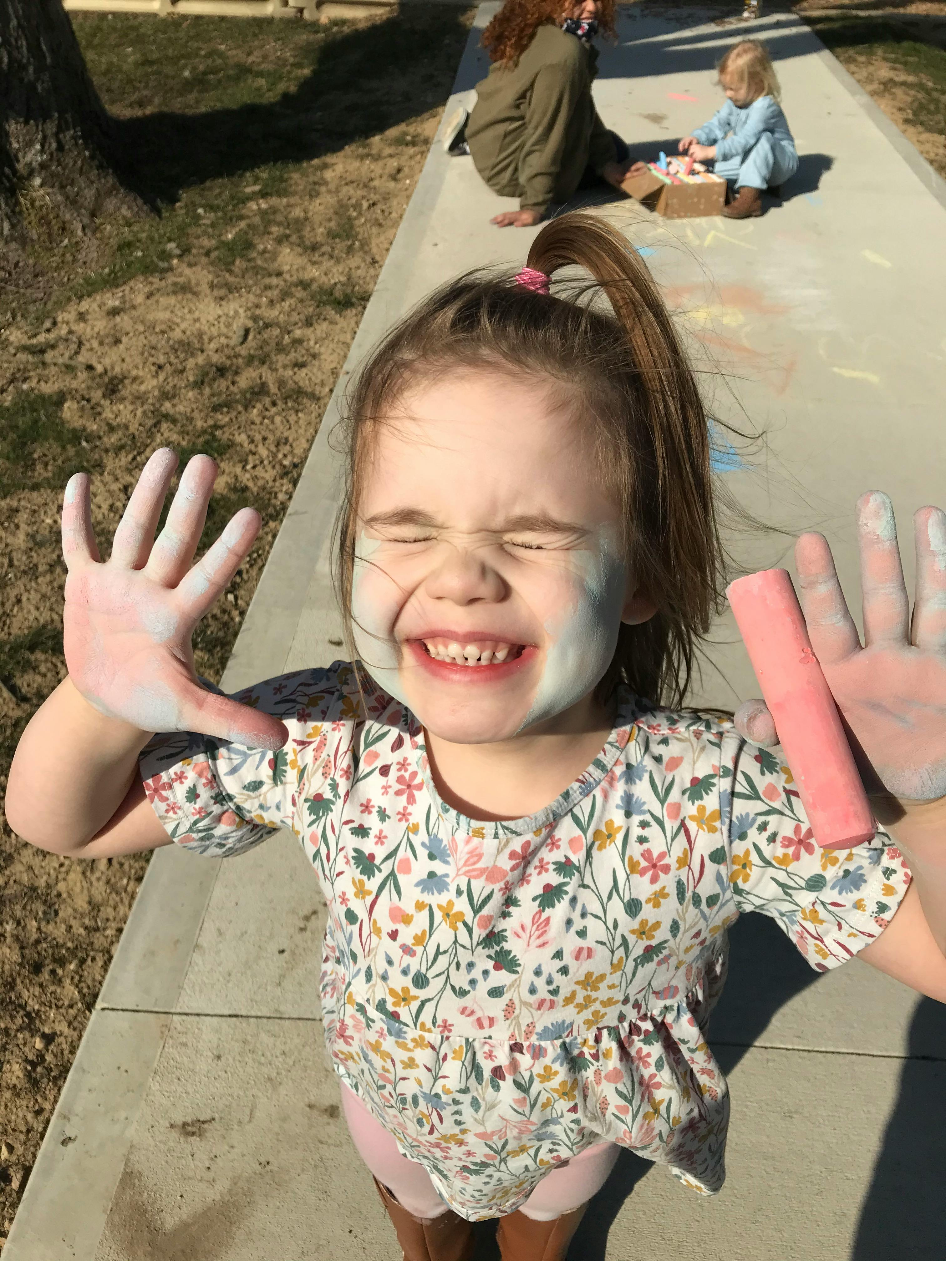 Child with chalk on face and hands holding pink chalk