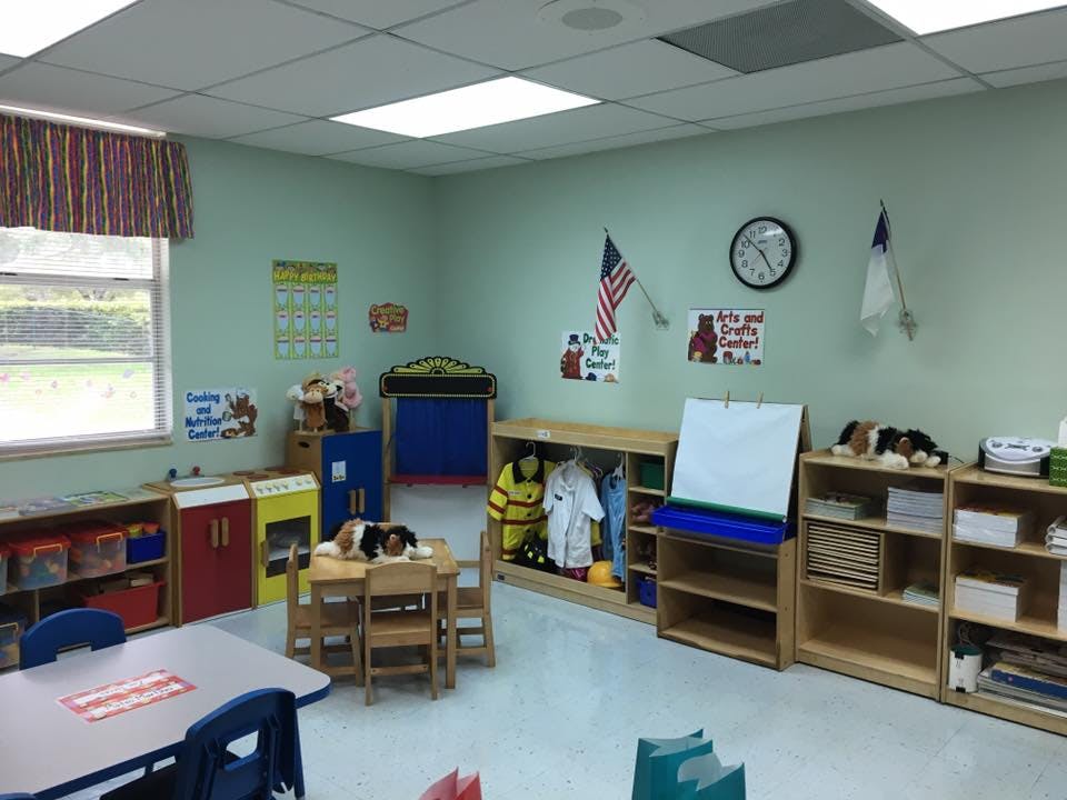 Empty classroom with small tables and chairs, shelves, and a window