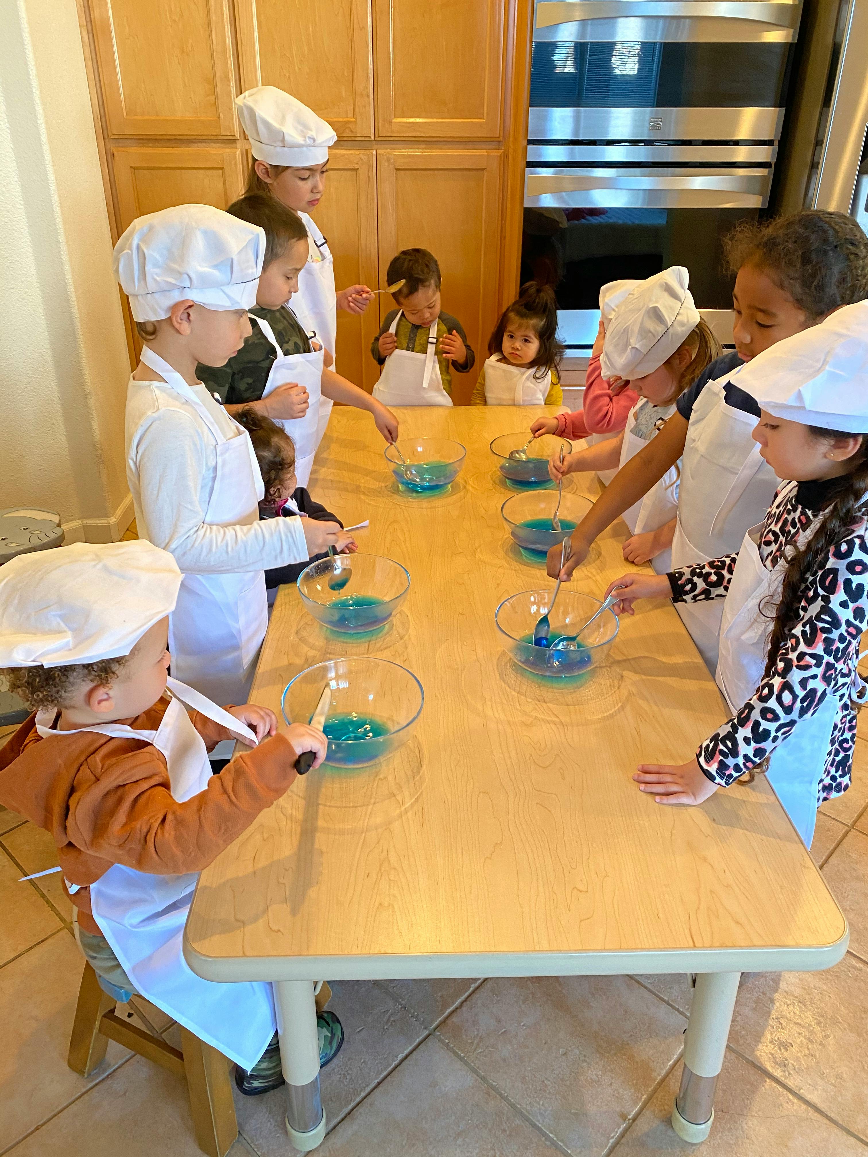 Children in chef hats and aprons mixing ingredients in bowls at a table