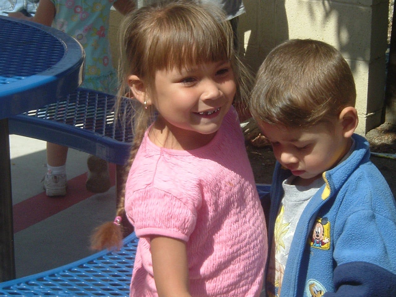 Two children standing together, one looking forward and one looking down
