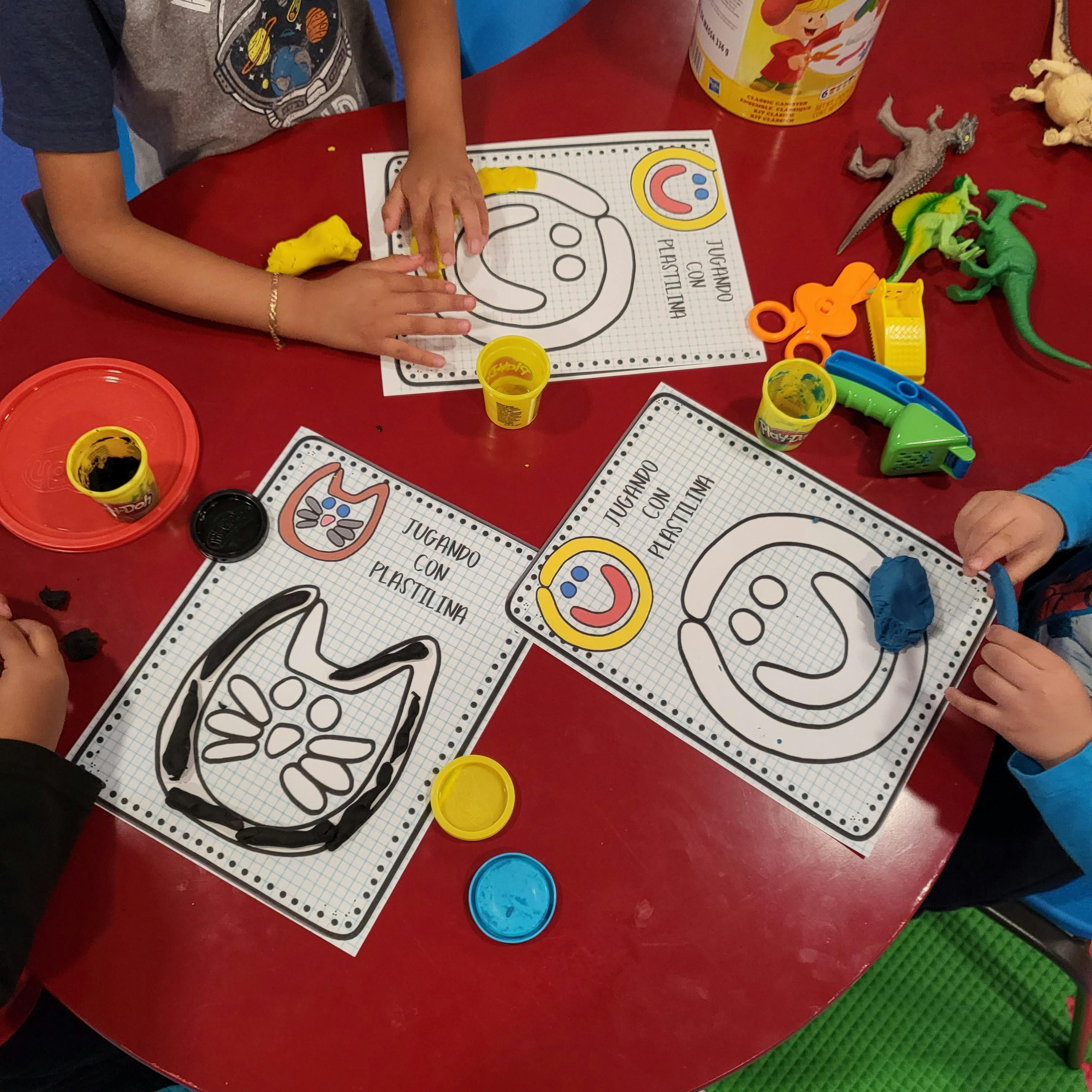 Children playing with playdough and activity mats at a red table