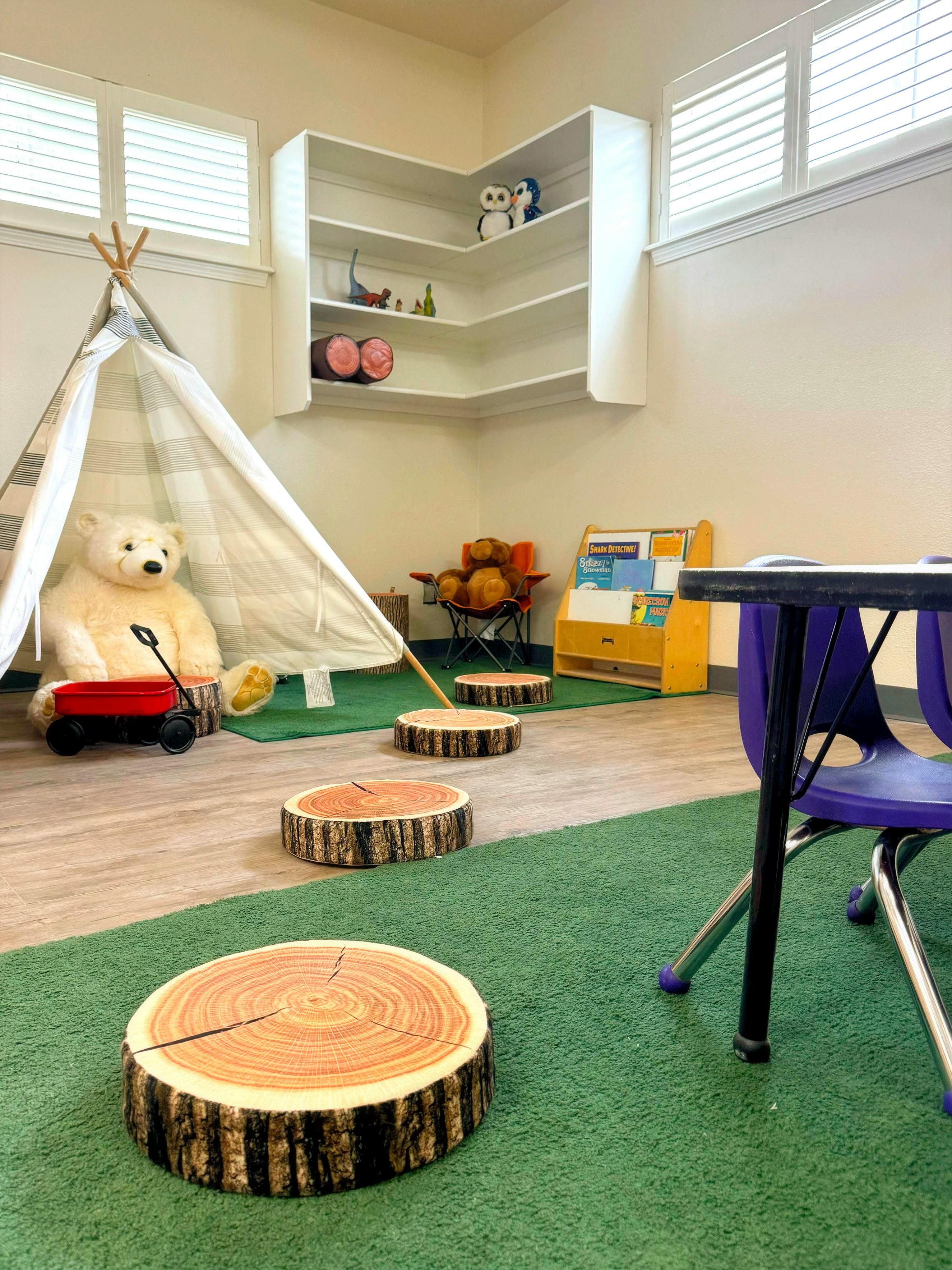 Playroom with a teepee, stuffed bear, and log-shaped floor cushions