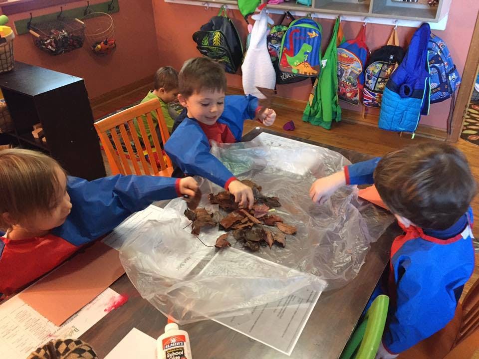 Three children playing with leaves and glue on a table