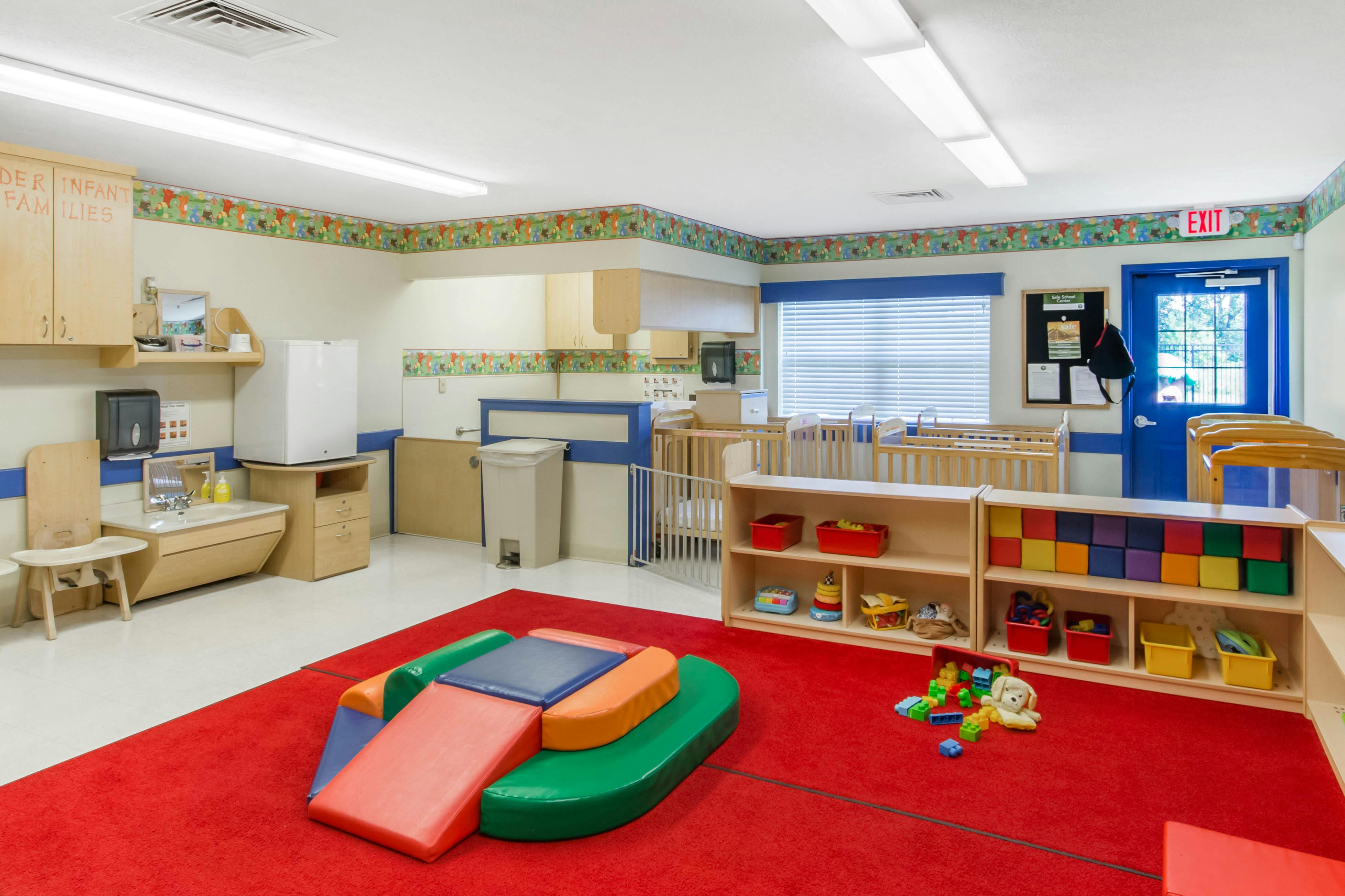 Childcare room with a play mat, cribs, sink, and exit door
