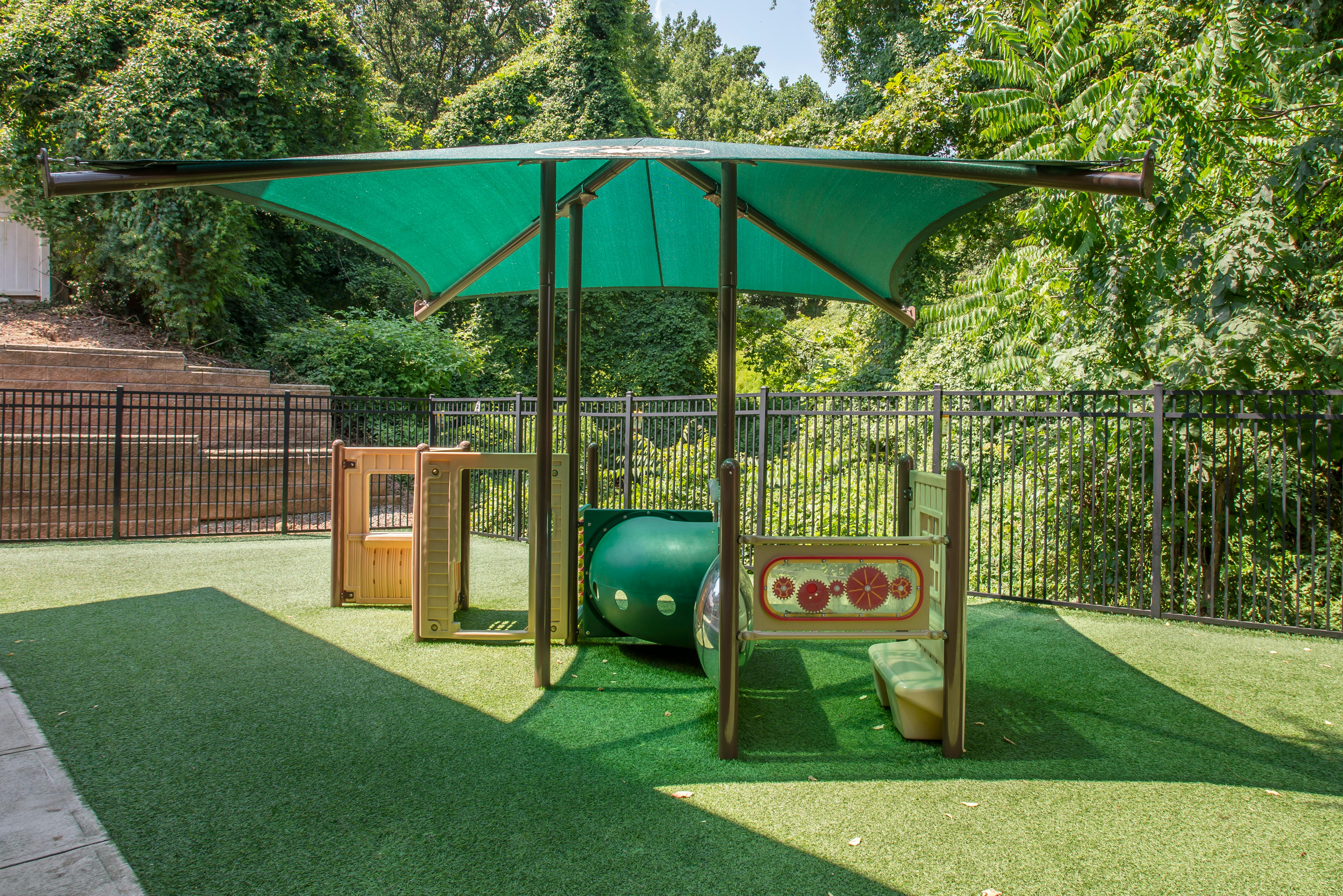 A children's playground with a green canopy, artificial turf, and climbing structures