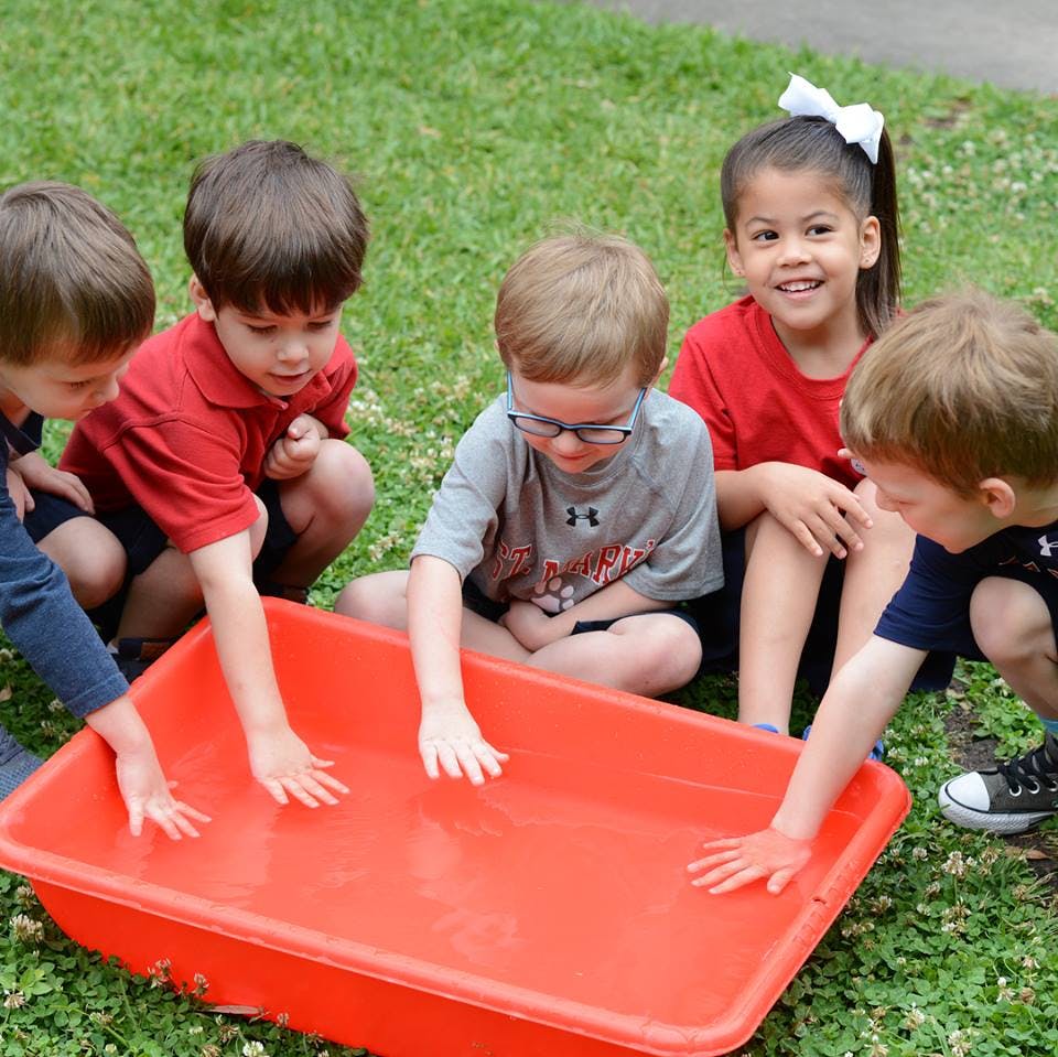 Children playing with water in a red bin outdoors