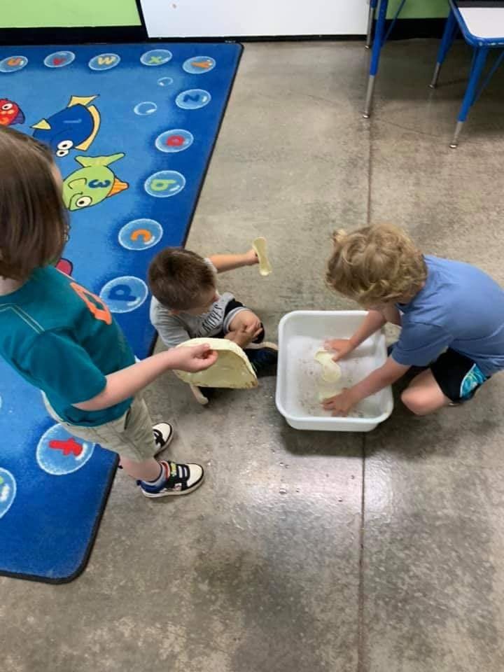 Three children playing with water in a classroom