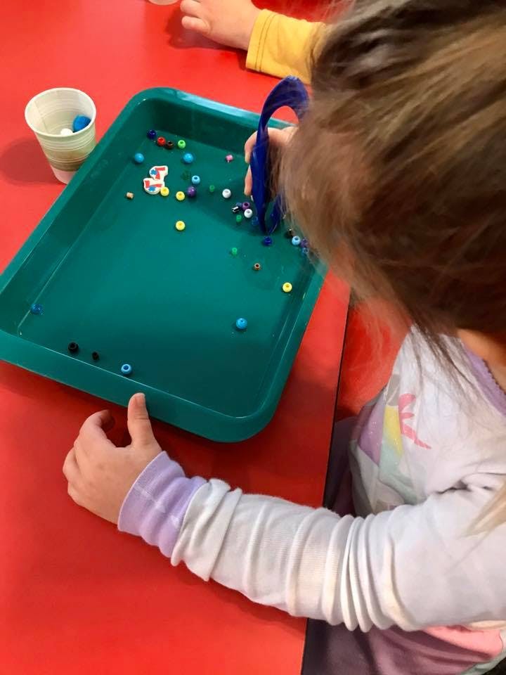 Child playing with beads in a green tray