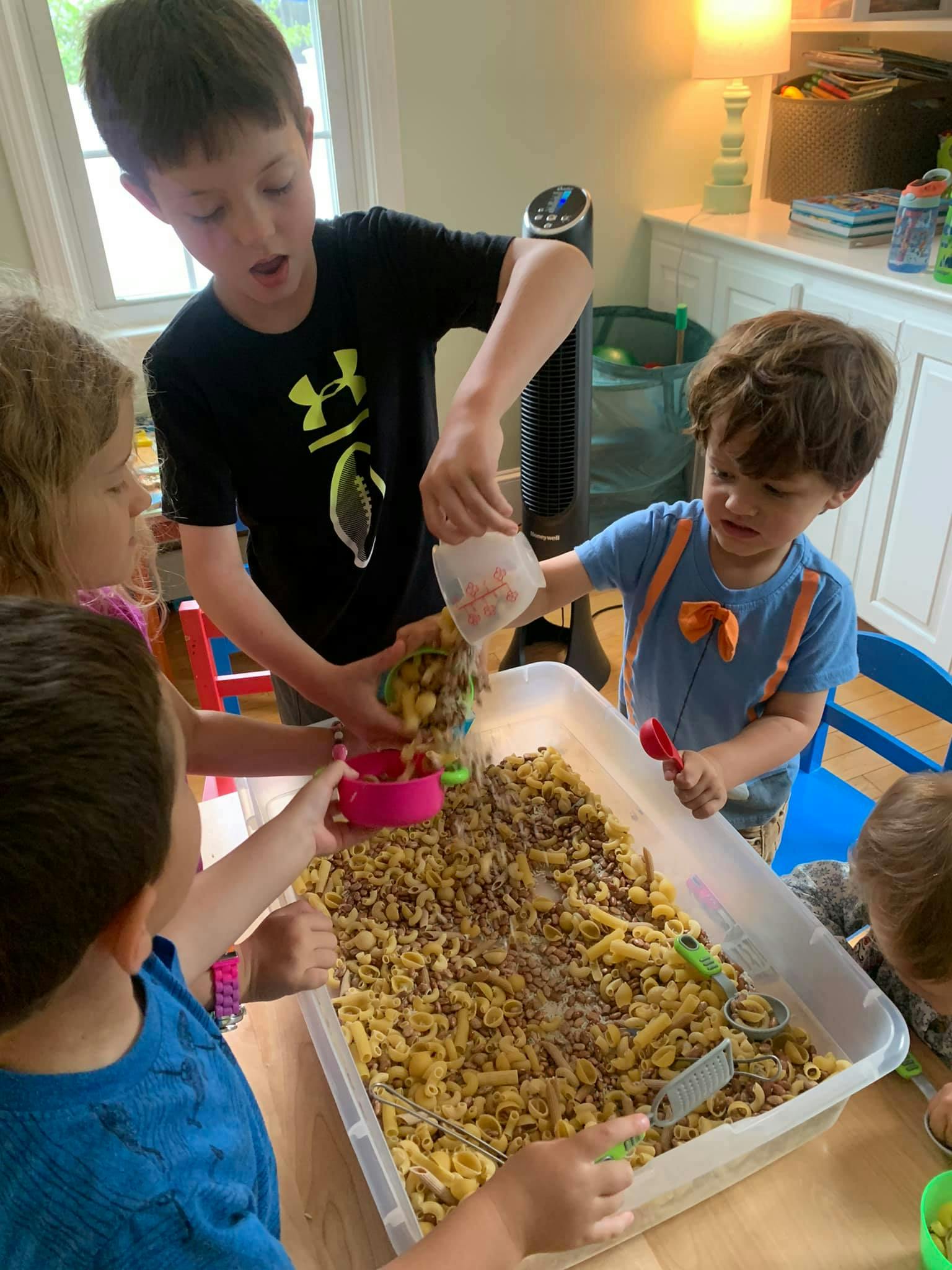 Children playing with pasta and beans in a large bin