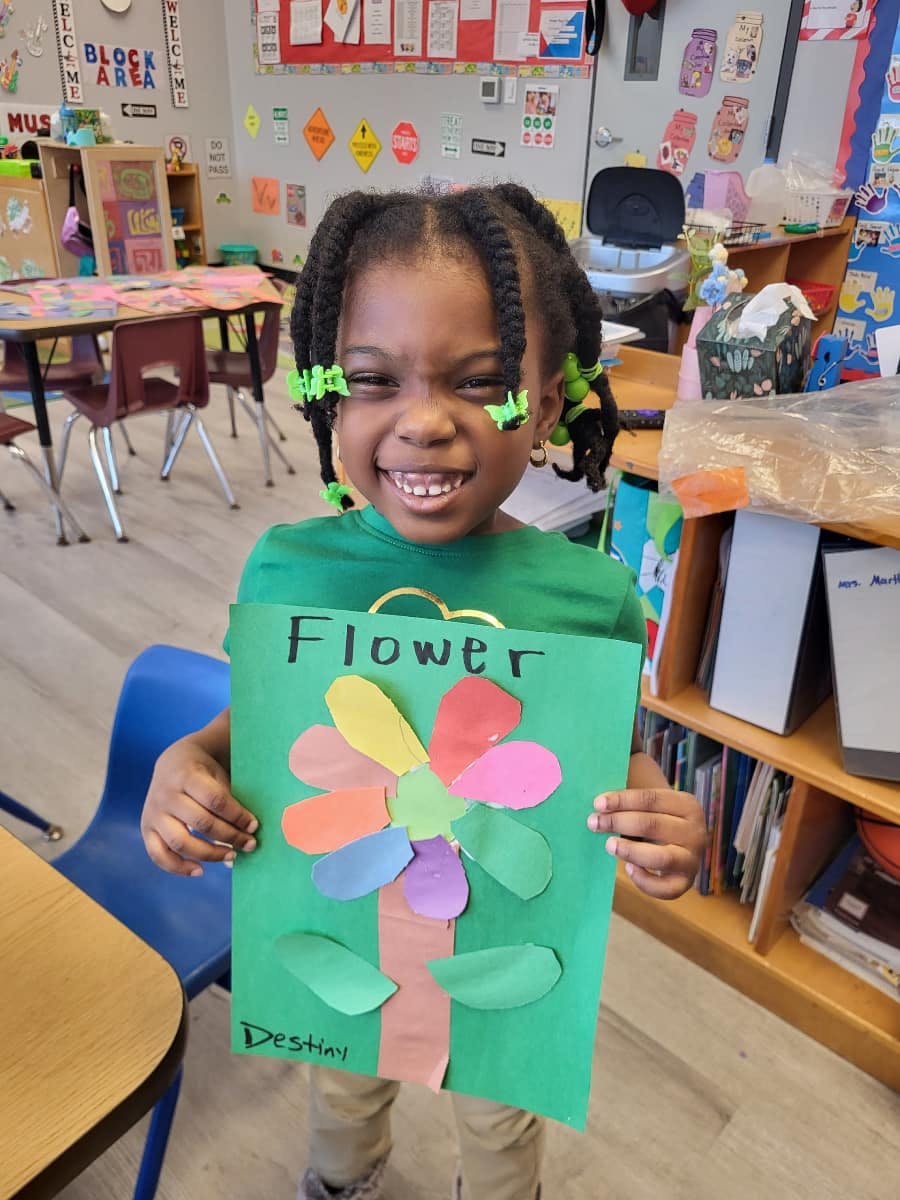 Child holding up a green paper craft with "Flower" written on it