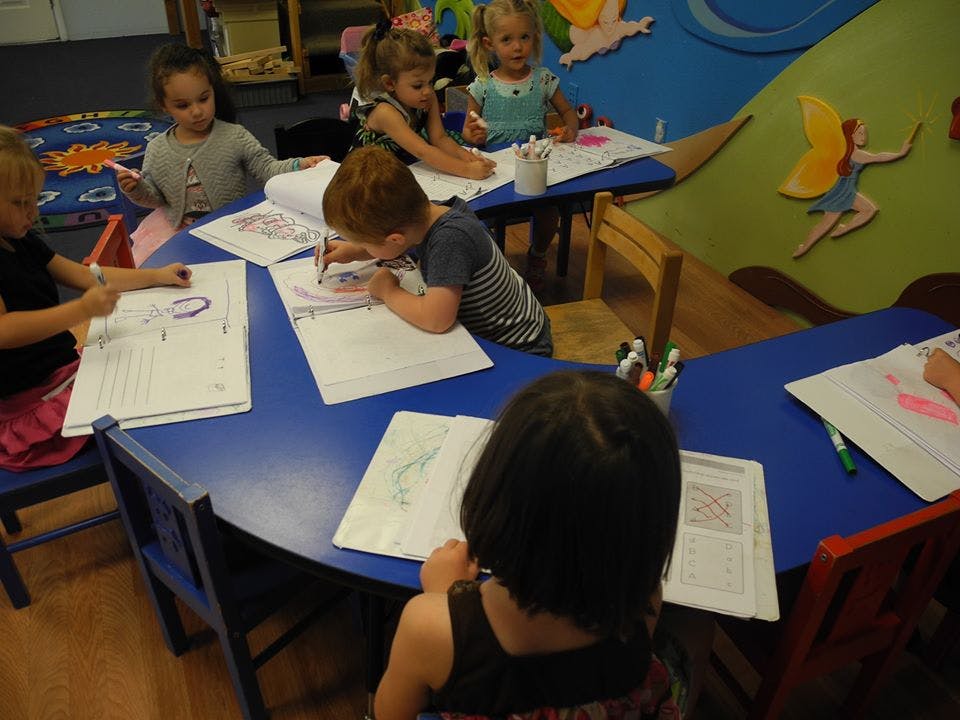 Children drawing and writing at blue tables in a classroom