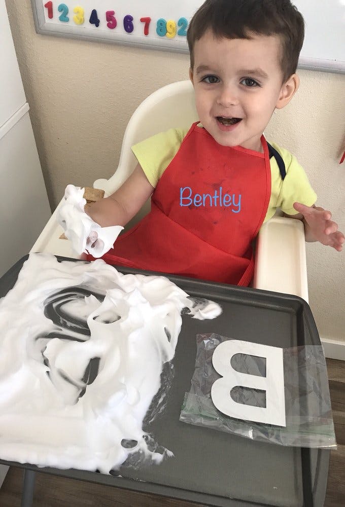 Child in high chair playing with shaving cream and a letter B cutout