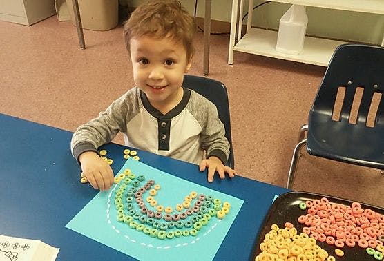 Child making a rainbow craft with colorful cereal pieces