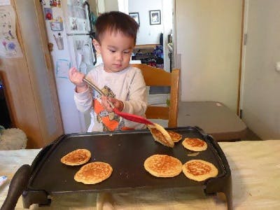 Child flipping pancakes on a griddle