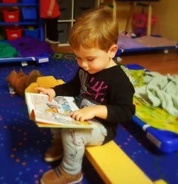 Child sitting on a yellow bench reading a book