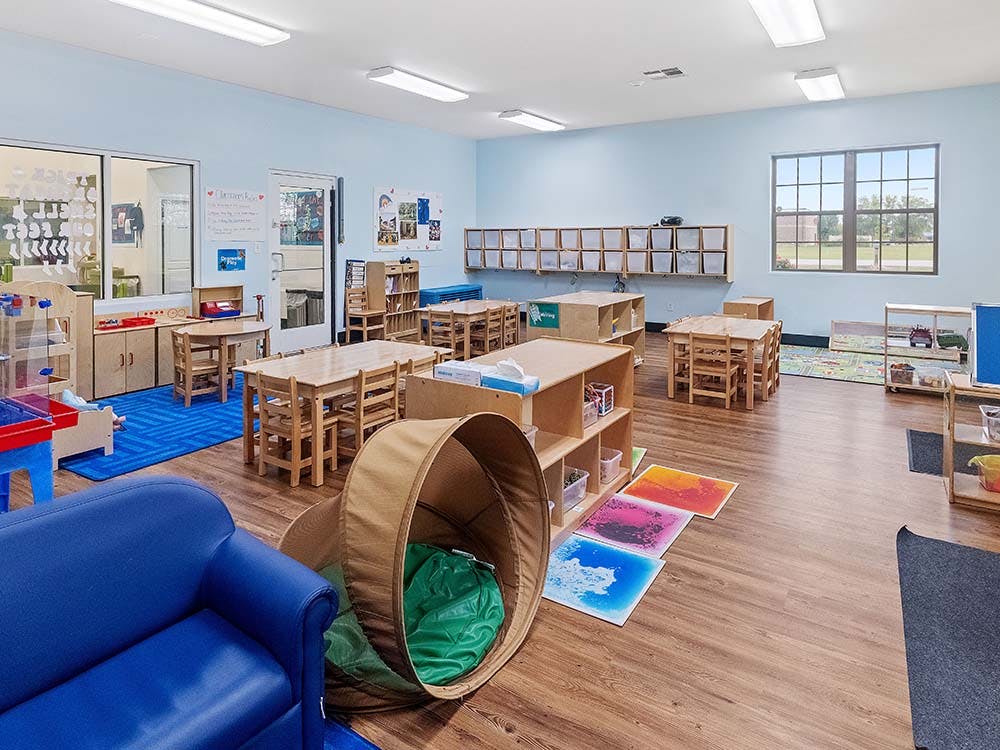 Classroom with small wooden tables and chairs, a blue couch, and storage shelves