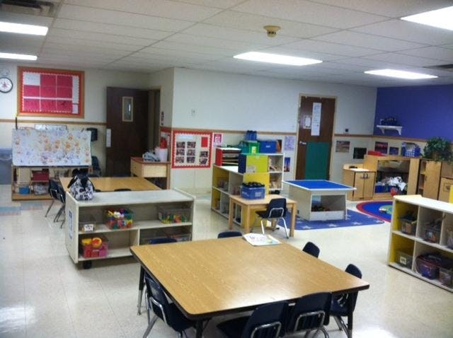 Empty classroom with small tables and chairs, shelves with toys, and posters on walls