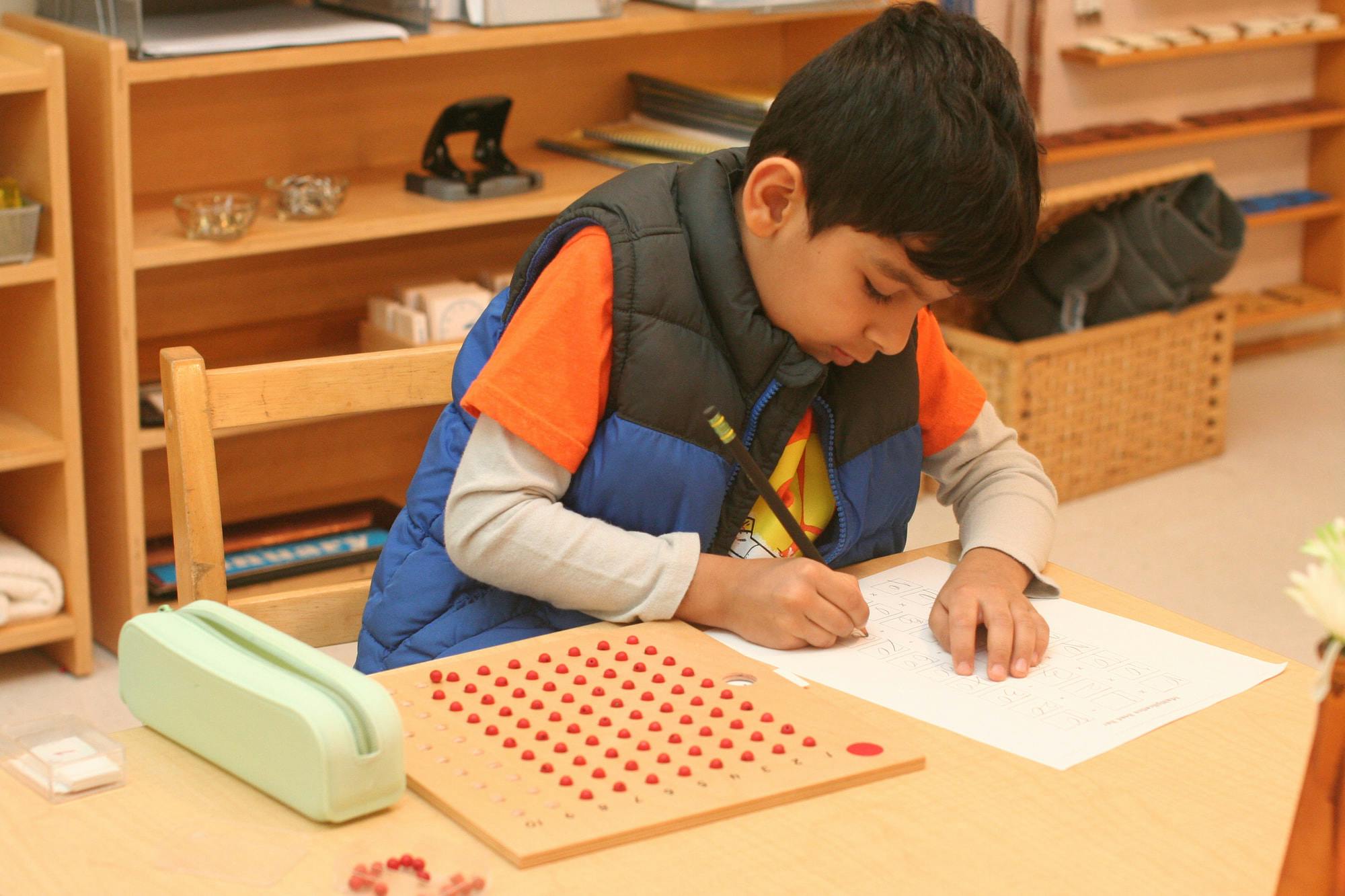 Child writing on paper at a table in a classroom