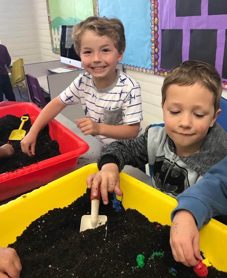 Two children playing with soil in plastic bins