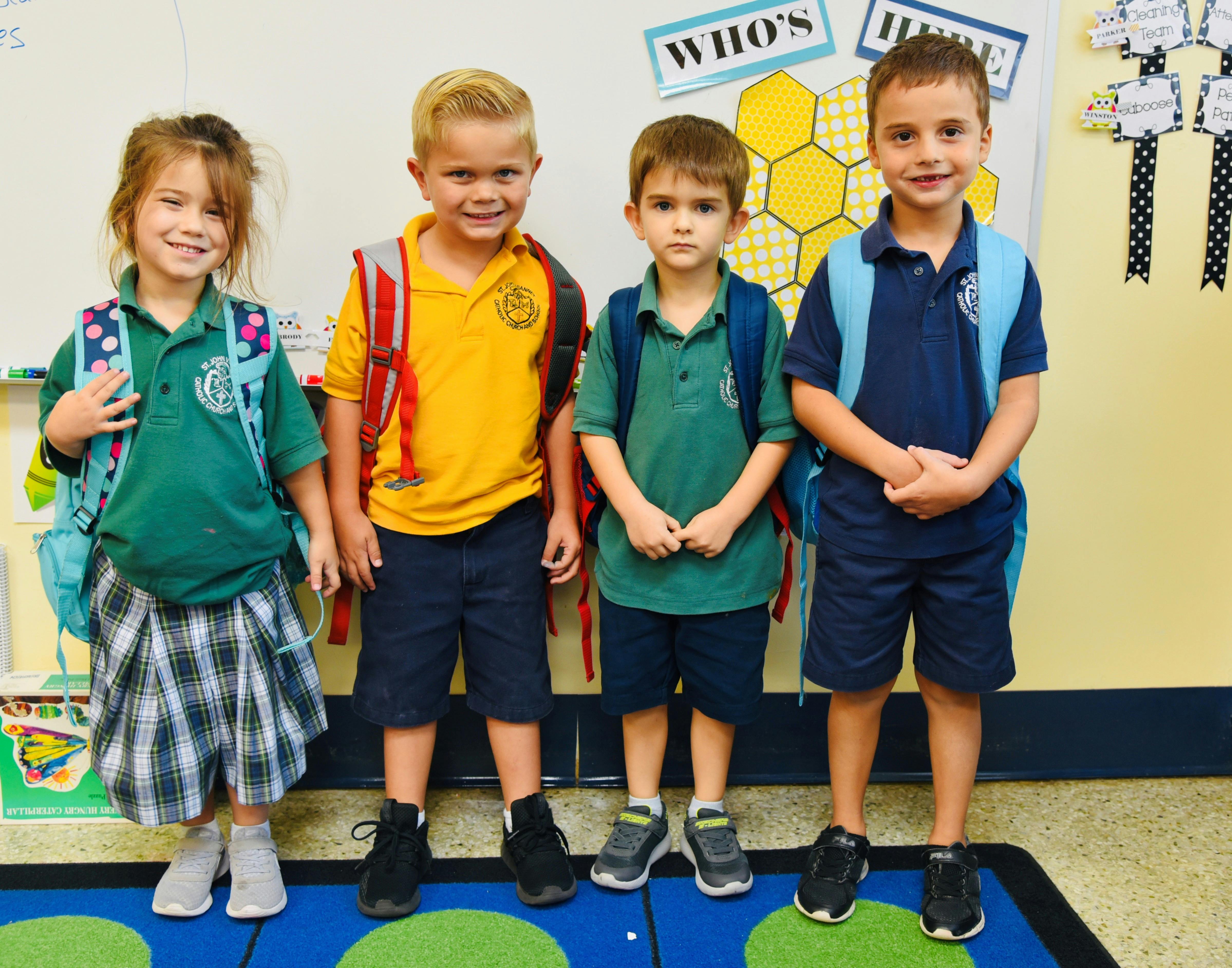 Four children wearing backpacks standing in a classroom