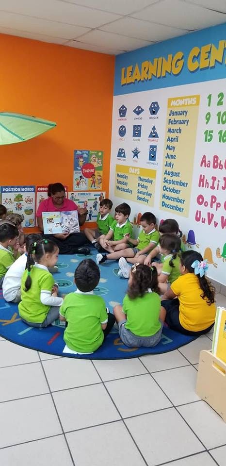 Adult reading a book to a group of children in a classroom