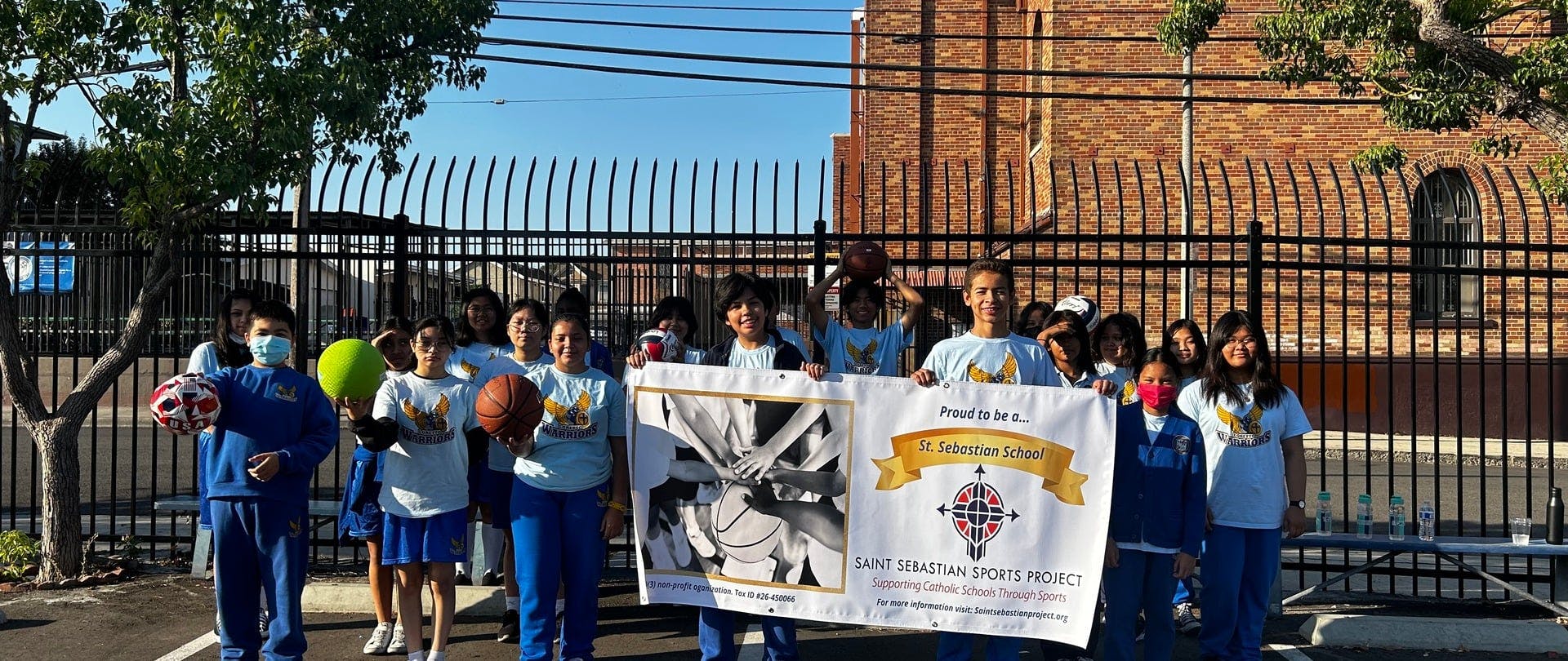 Group of children holding sports balls and a banner for St. Sebastian School