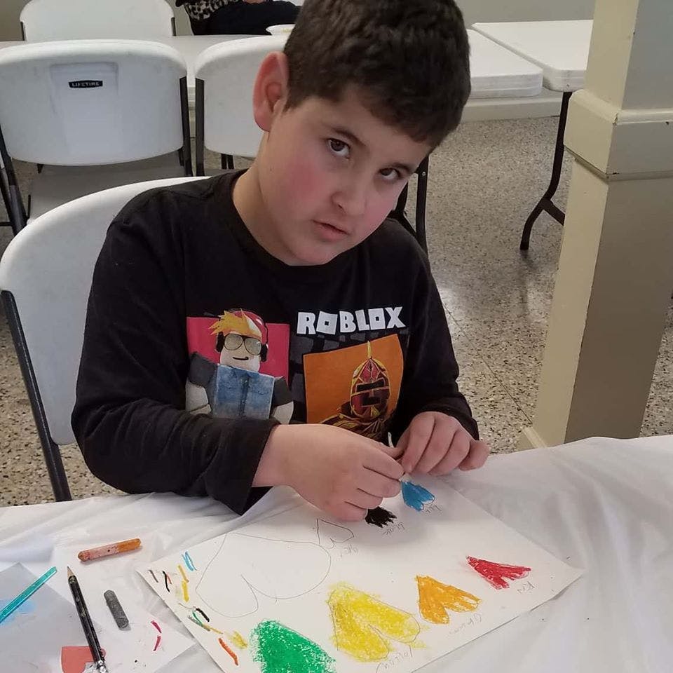 Child in a Roblox shirt drawing at a table