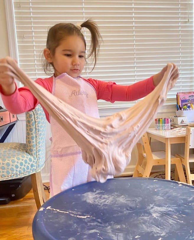 Child in an apron stretching slime over a table
