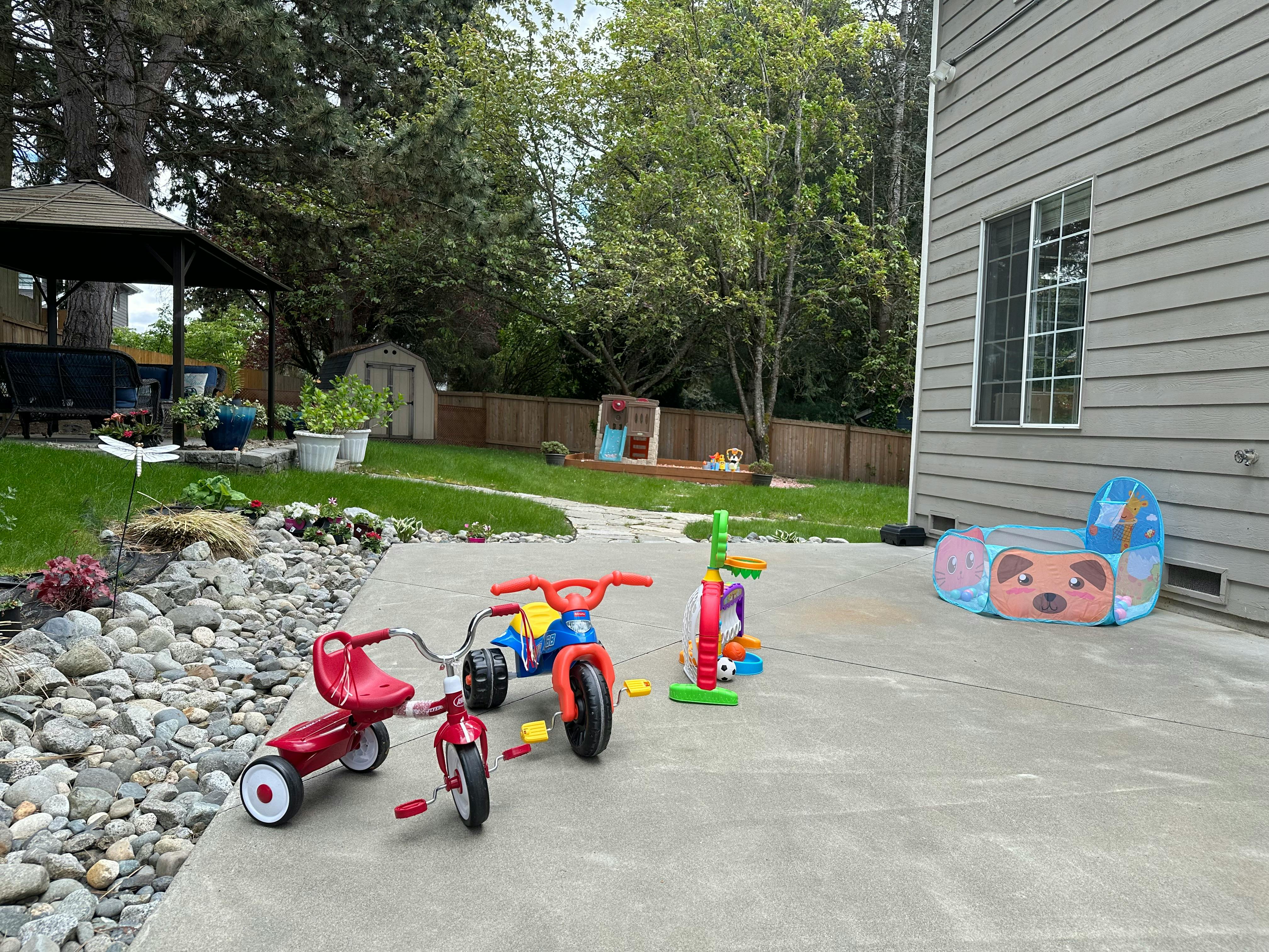 Children's tricycles and toys on a patio next to a house