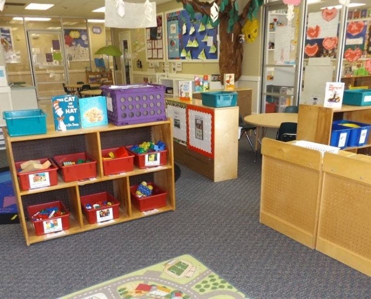Classroom with wooden shelves holding red bins of toys and books