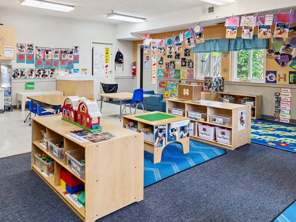 Classroom with tables, chairs, storage shelves, and child artwork