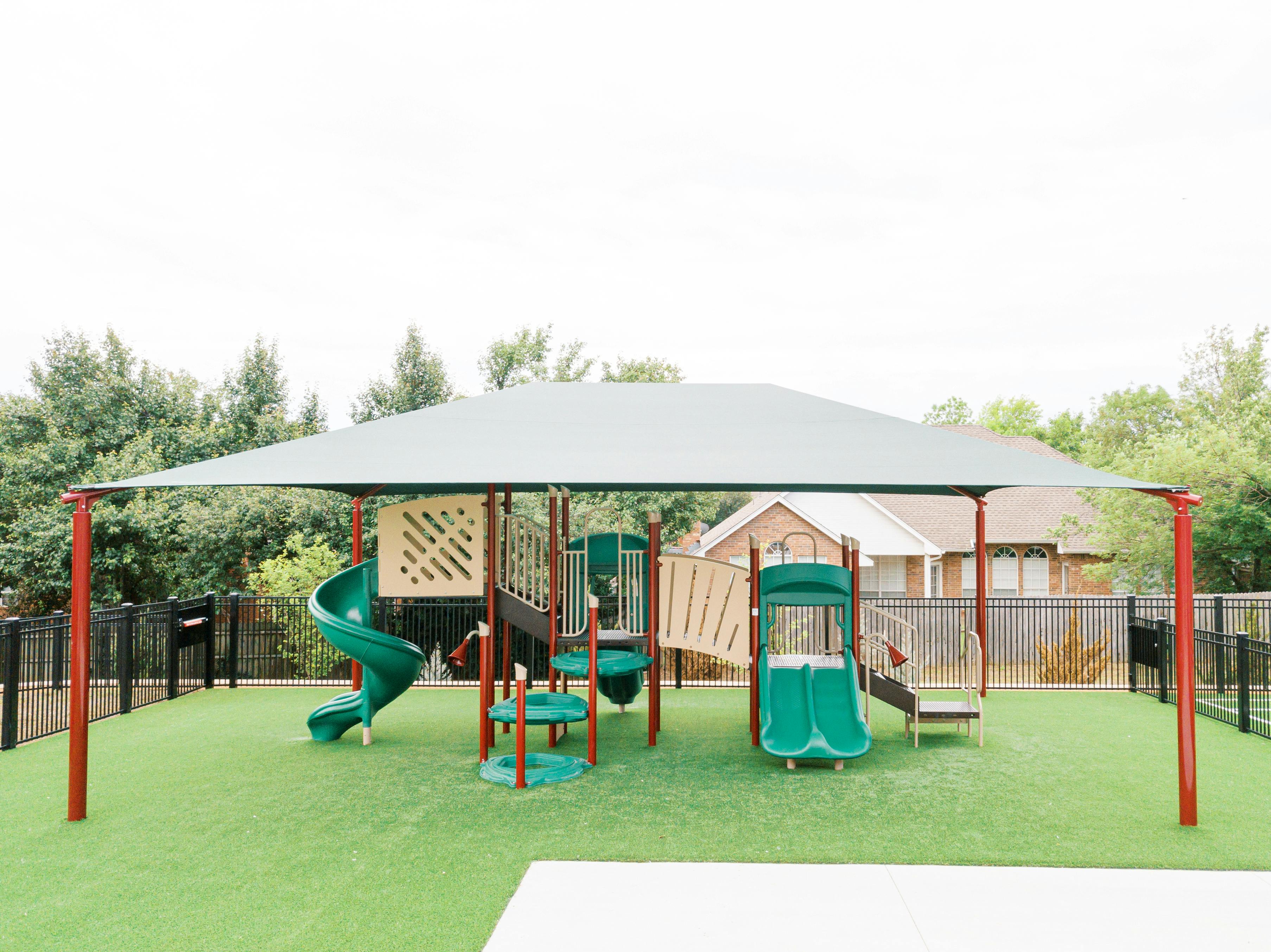 Playground with green slides and climbing structures under a shade canopy