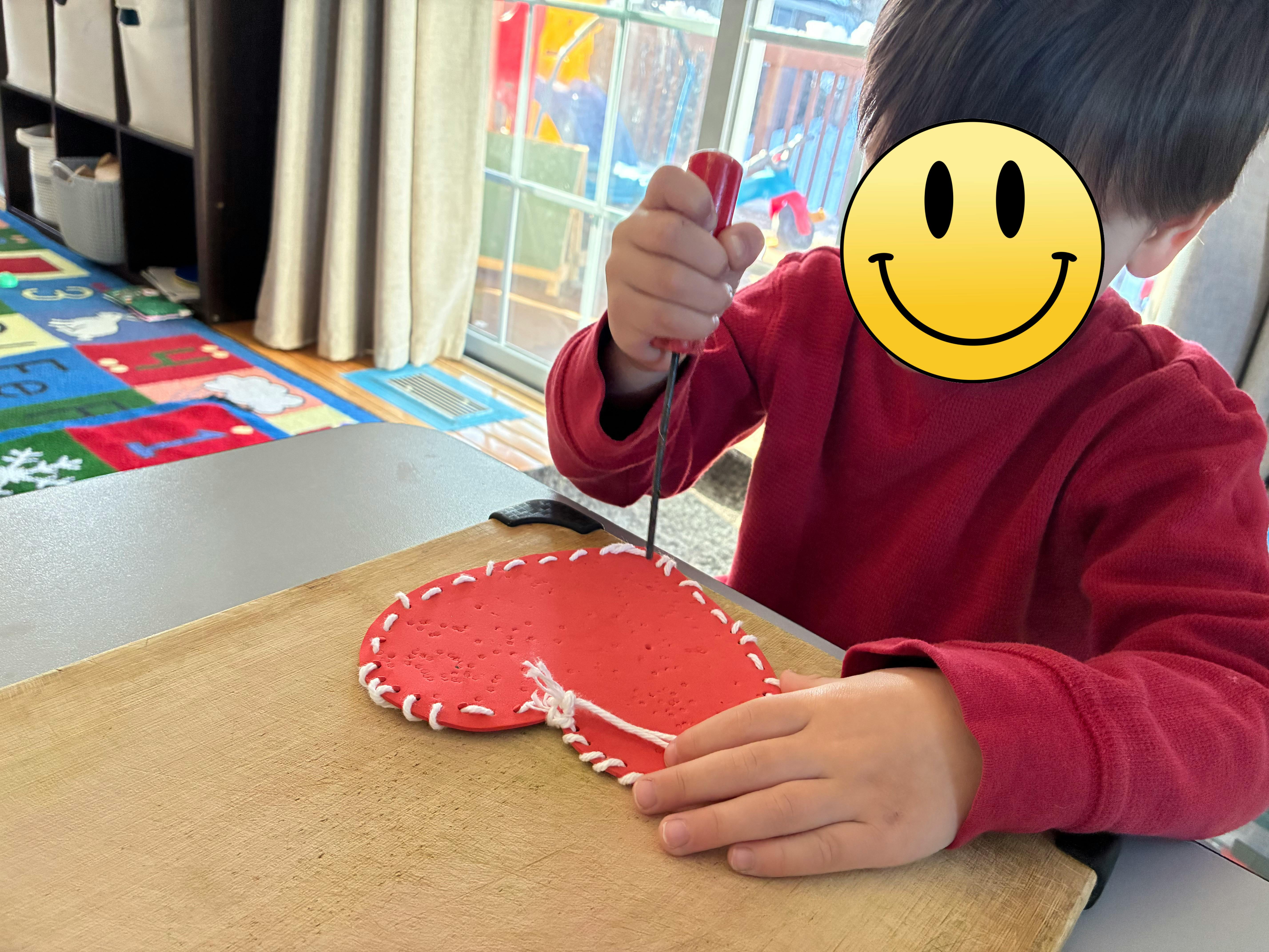 Child using a punching tool on a heart-shaped craft at a table