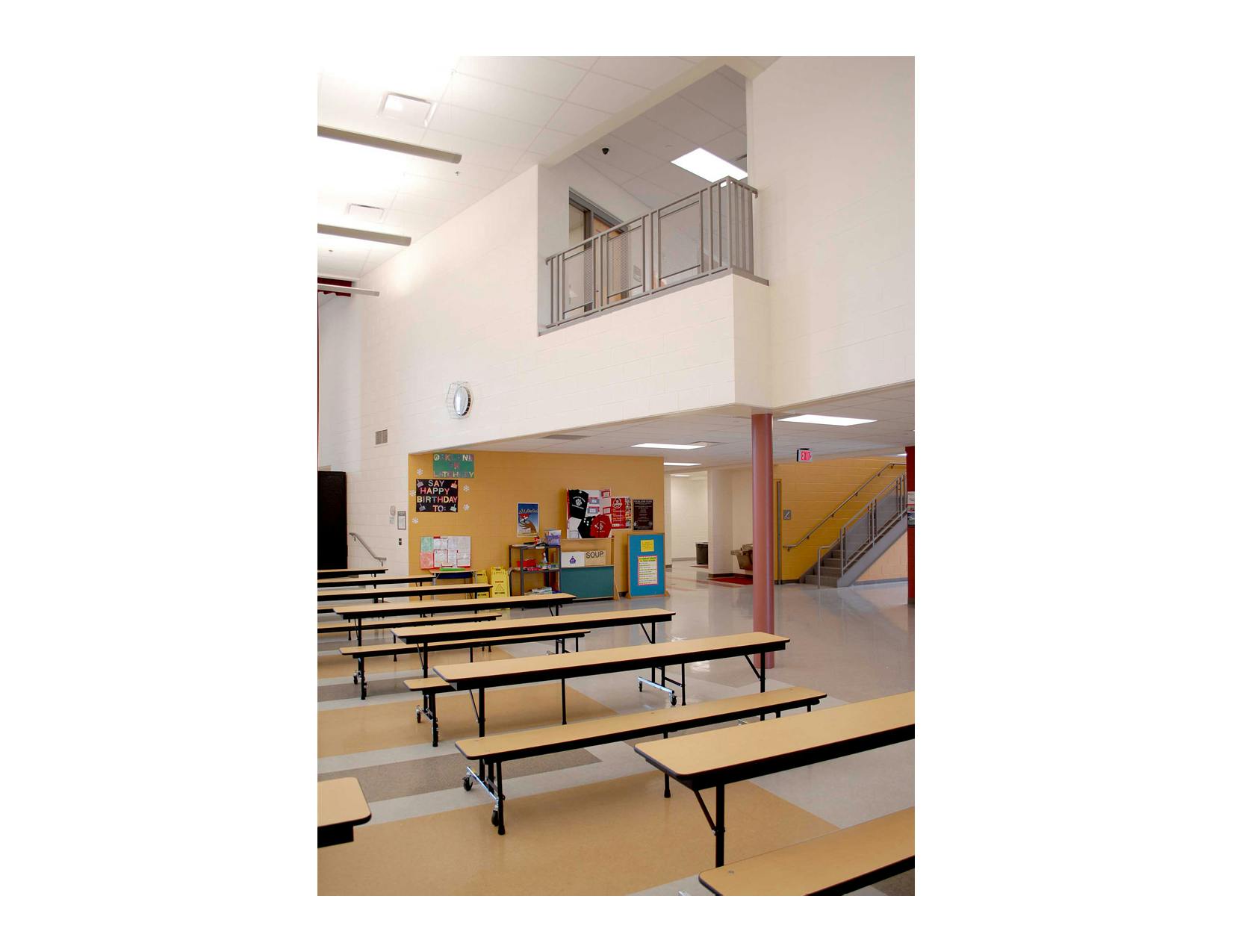 Empty cafeteria with long tables and benches, a balcony overhead