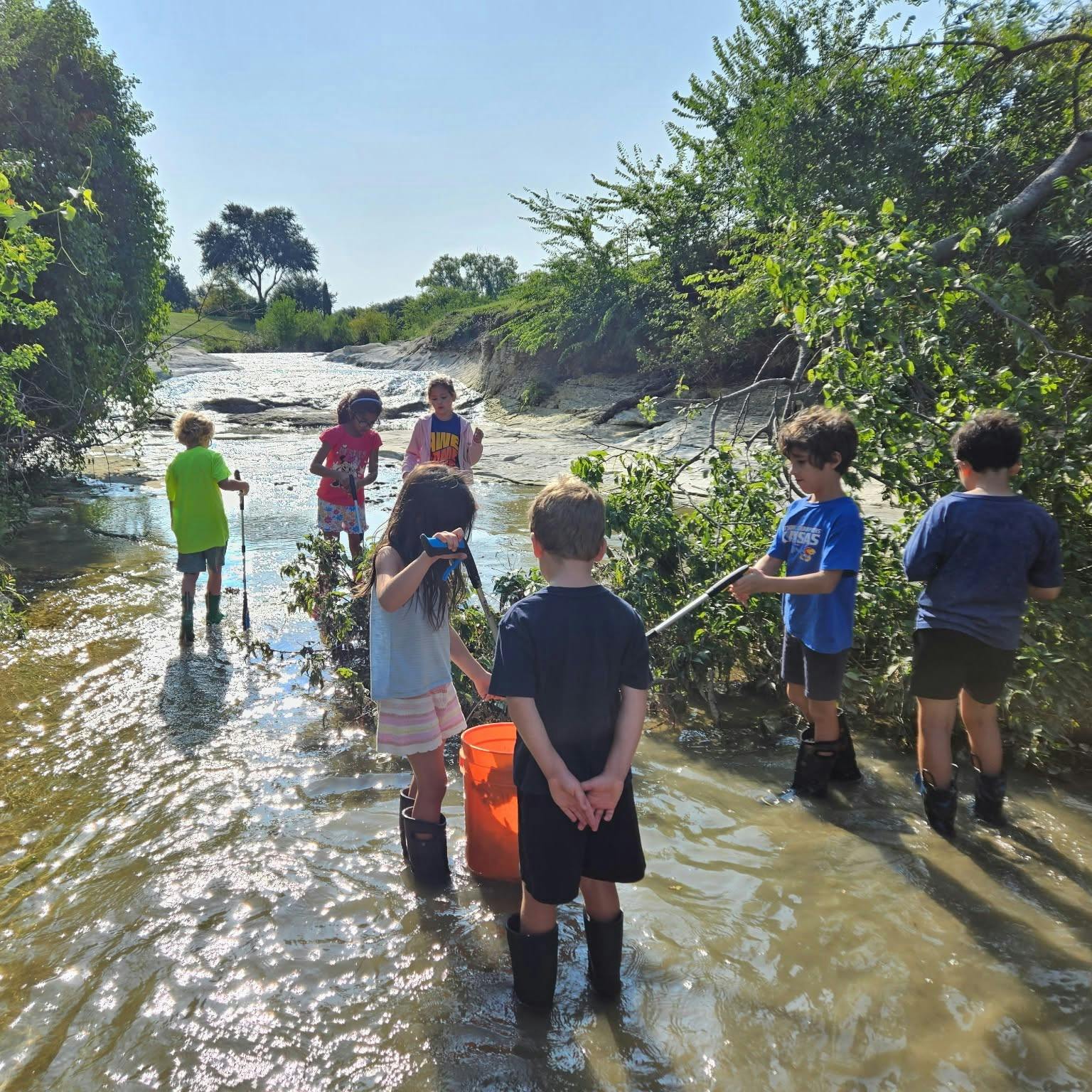 Children in boots playing and exploring in a shallow stream