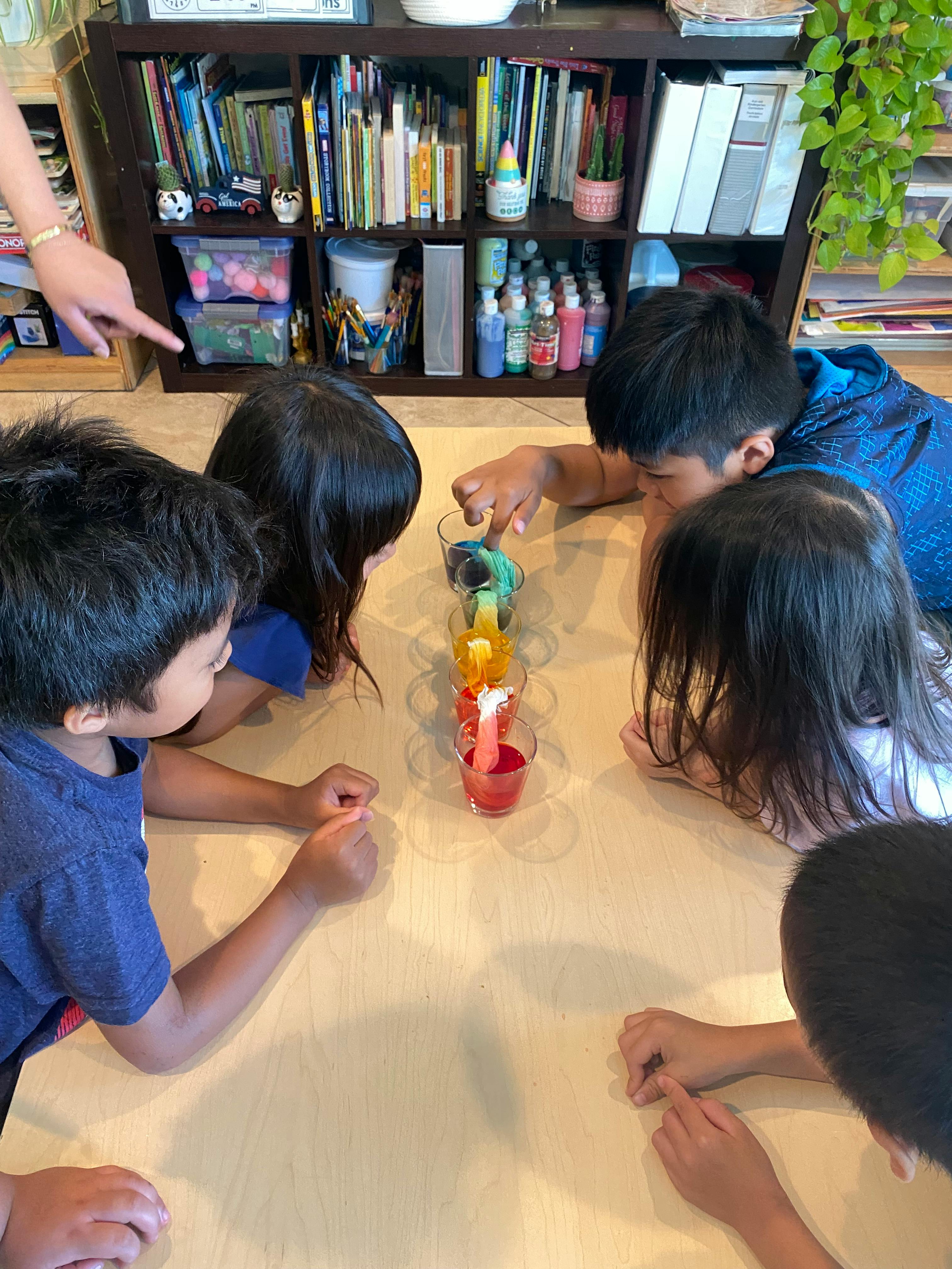 Children gathered around a table observing a science experiment with colorful liquids