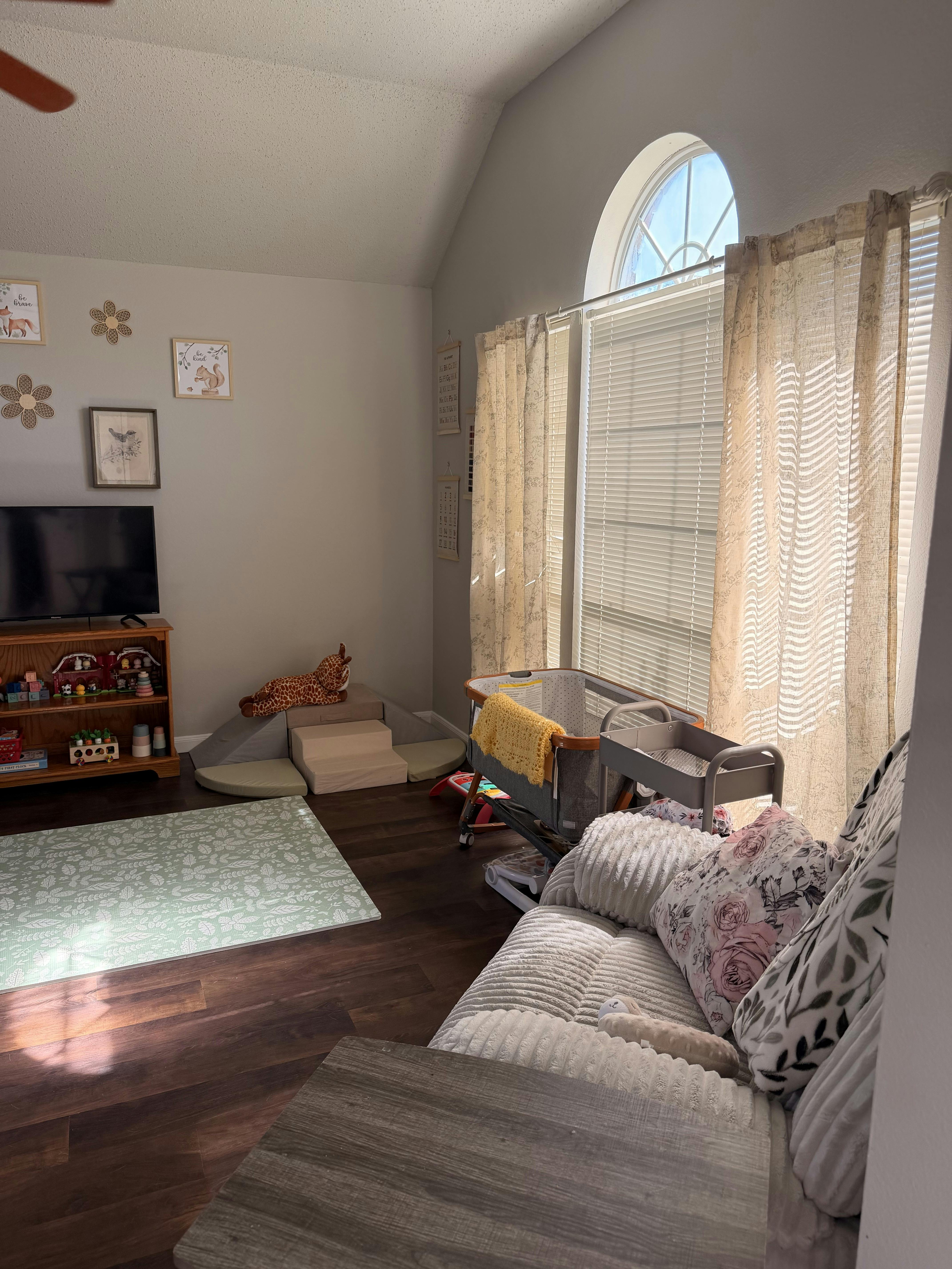 Living room with baby play area, crib, TV, and couch
