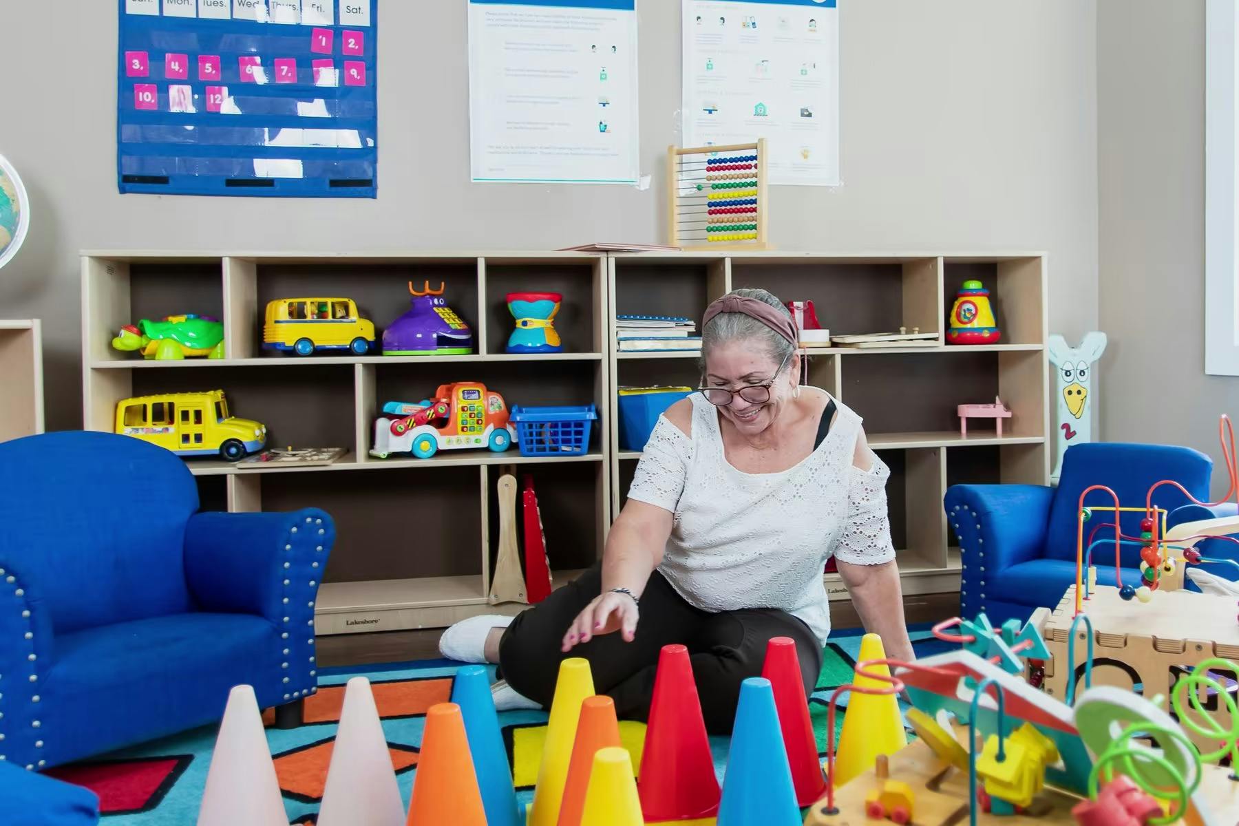 Person sitting on floor surrounded by colorful toys in a classroom