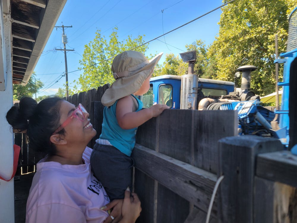 Person holding a child wearing a hat to look over a fence