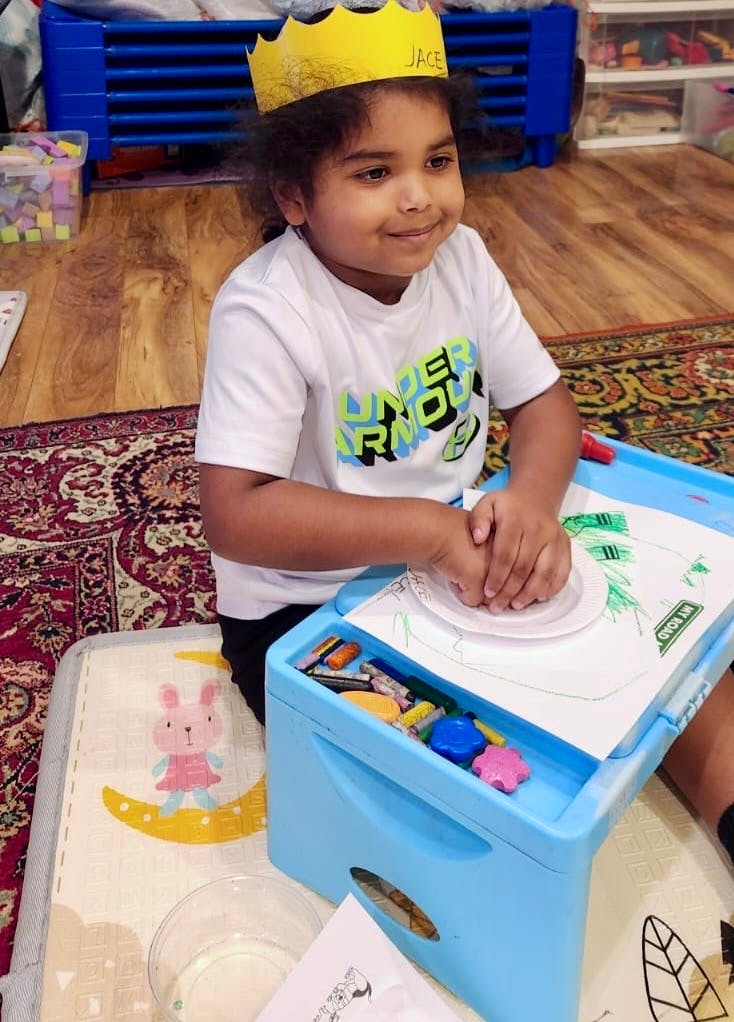 Child wearing a crown and drawing at a small table