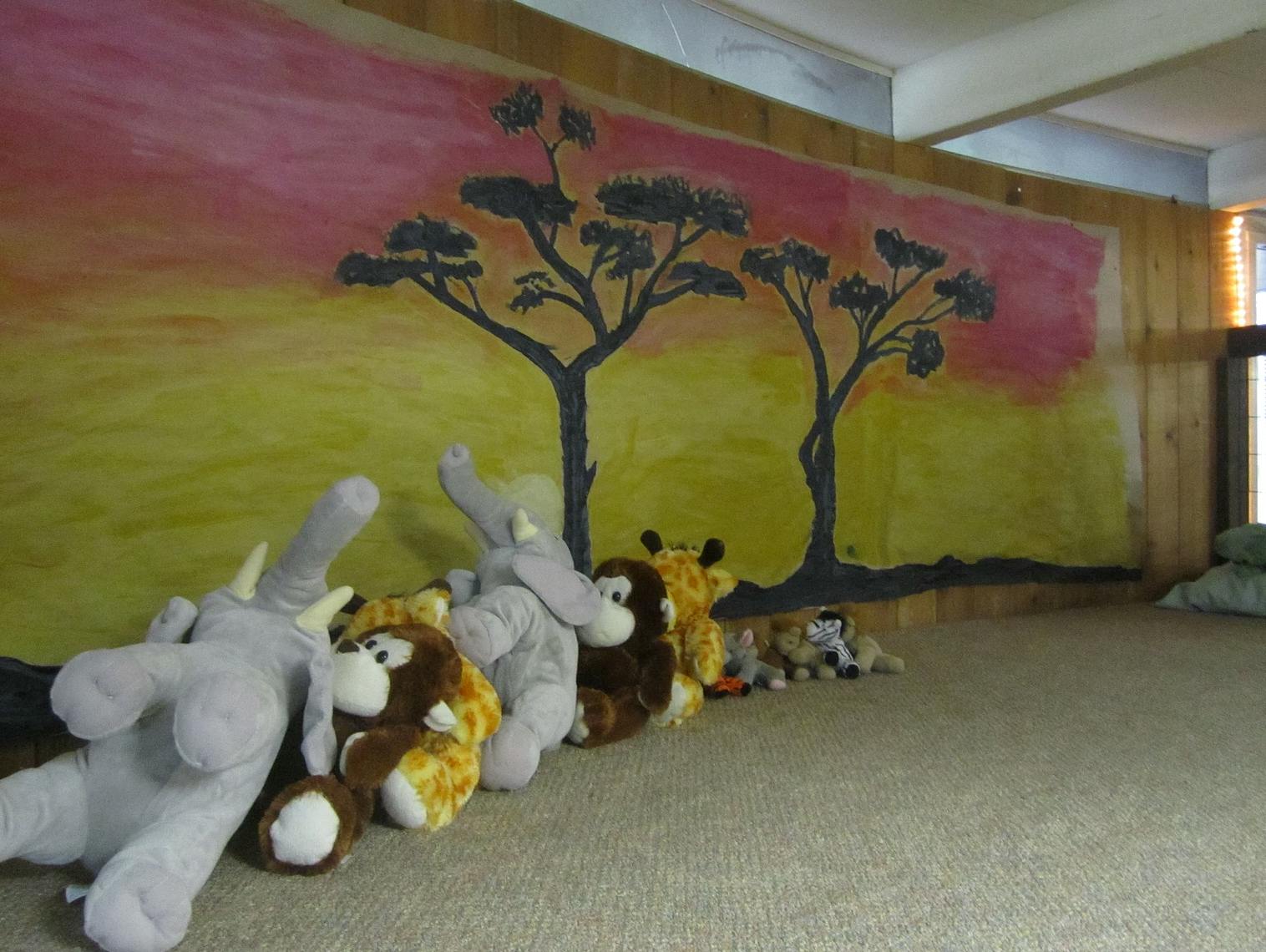 Stuffed animals lined up against a wall with a painted safari scene