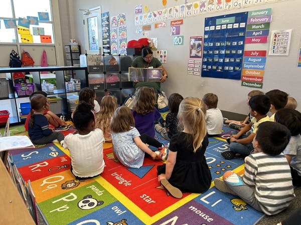 Adult reading a book to children sitting on a colorful alphabet rug in a classroom
