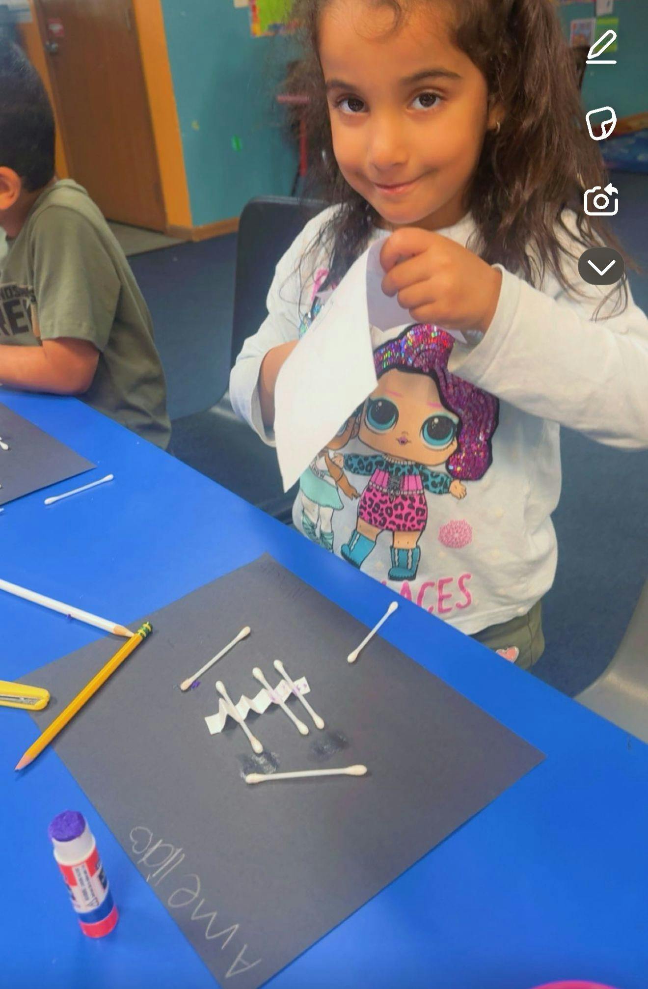 Child smiling while doing a craft at a blue table